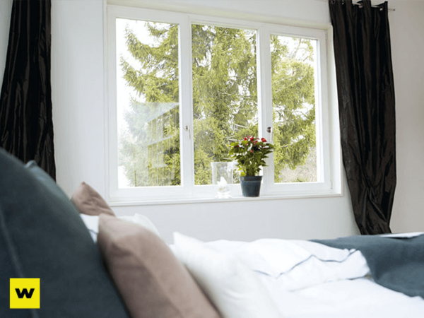 Helles Schlafzimmer mit großem Fenster, Blick ins Grüne und Topfpflanze auf der Fensterbank.