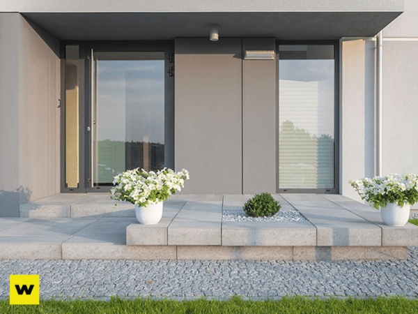 Moderner Hauseingang mit großen Glasflächen, Betonstufen und weißen Blumenkübeln.