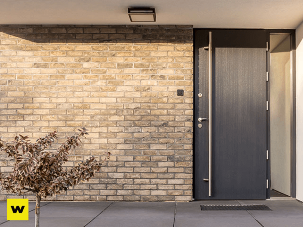 Moderne Haustür aus dunklem Material in einer hellen Klinkerfassade mit kleinem Vorgarten.